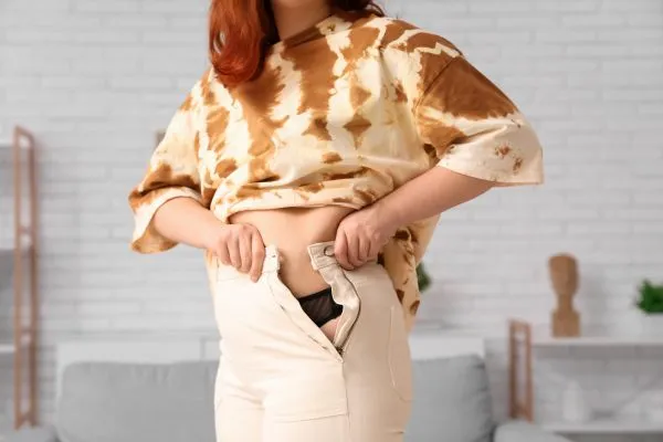 Image of woman trying to do her trousers up after pregnancy weight gain Earley