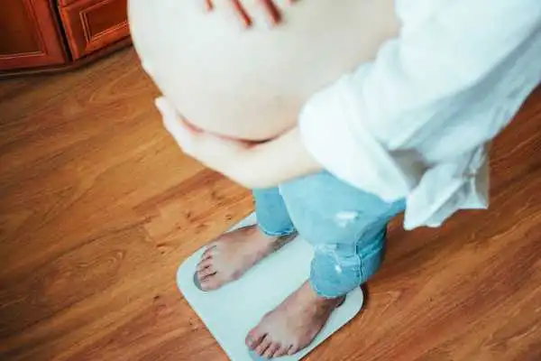 Image of woman weighing herself and experiencing weight gain through pregnancy Earley